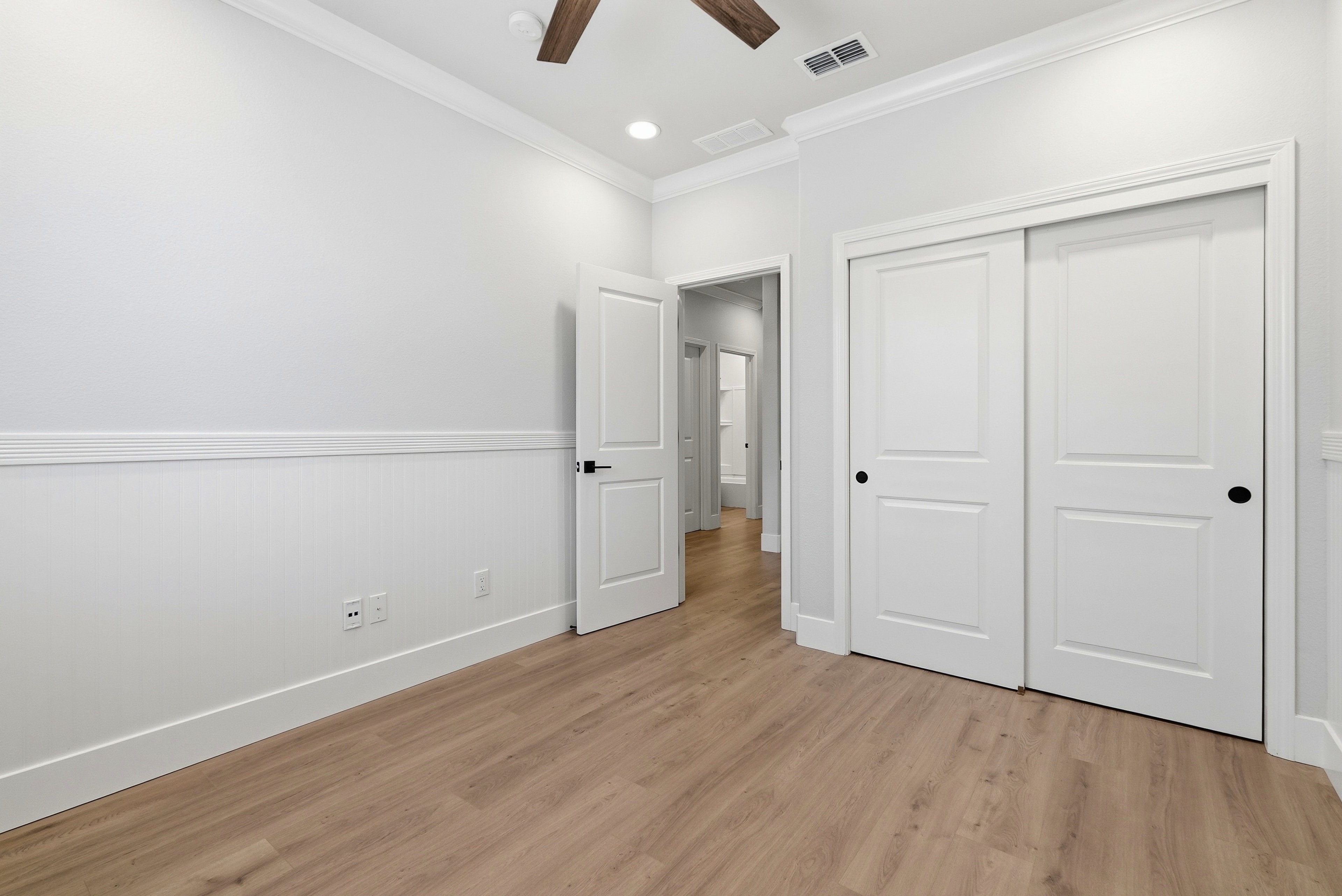 Bright bedroom with wood flooring, sliding closet doors and ceiling fan
