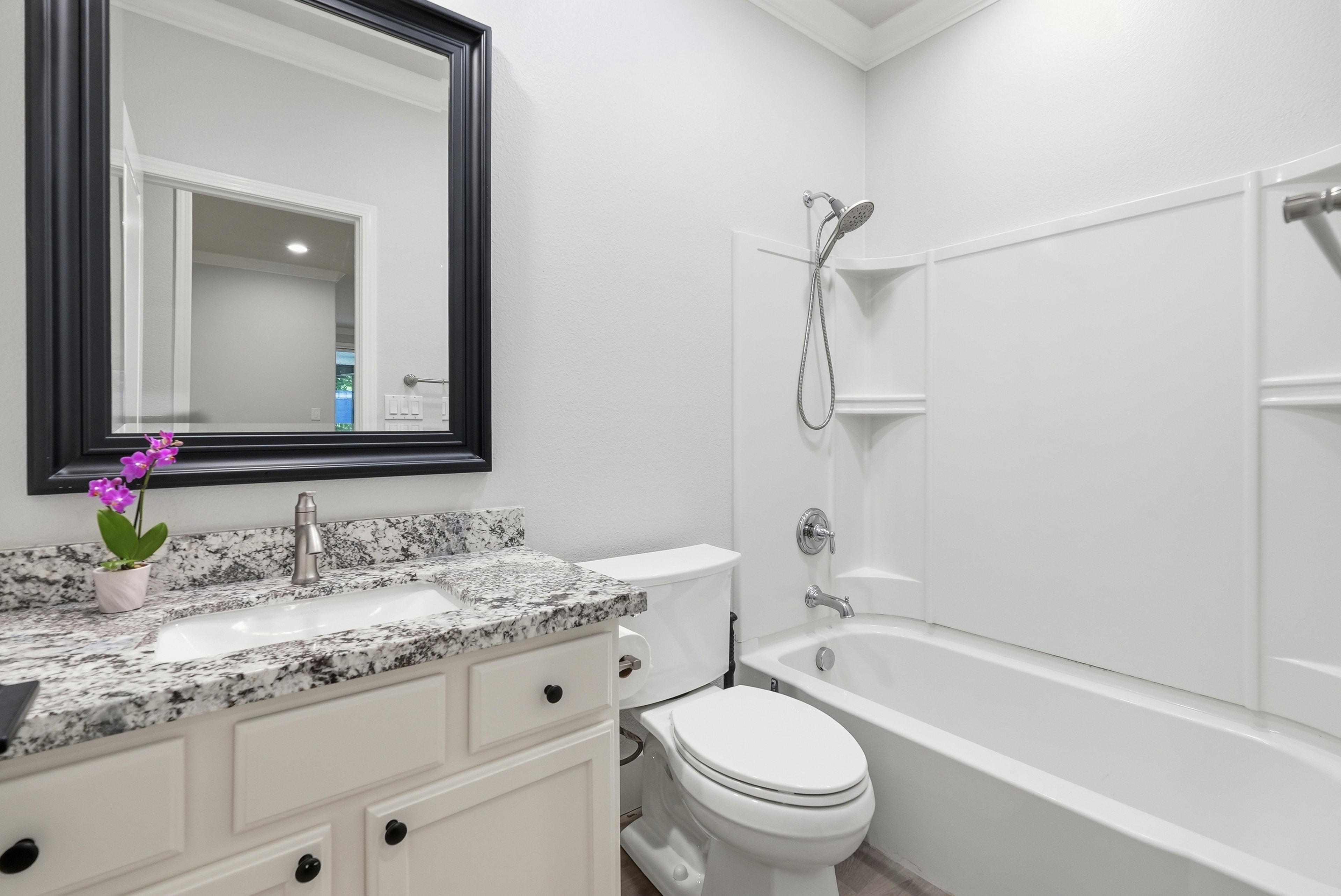 Hallway bathroom with granite countertop, white cabinetry and tub shower combo